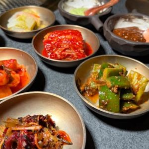 Variety of Korean banchan side dishes served in metallic bowls on a table.
